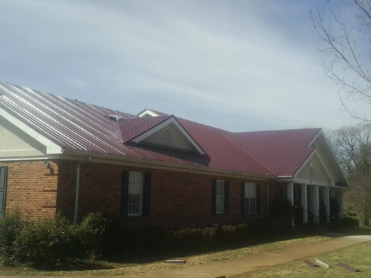 Red metal roof with gabled entries on a long brick building, from a Hail Damage Roof Repair job in Astoria
