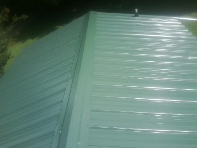 New green metal panels meeting at the ridge of a roof — Flat Roof Repair work by our crew in Astoria
