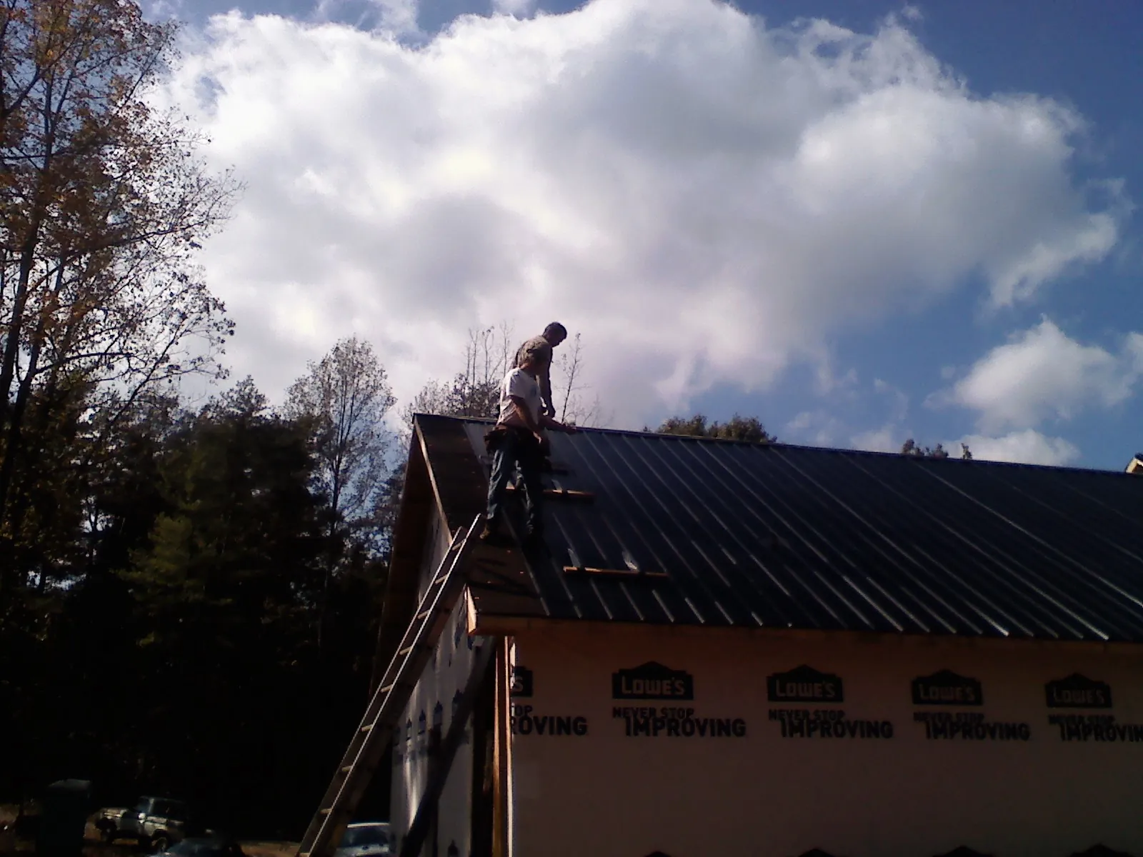 Roofer fastening dark metal panels high against a cloudy sky, from a Roof Inspection job in Astoria
