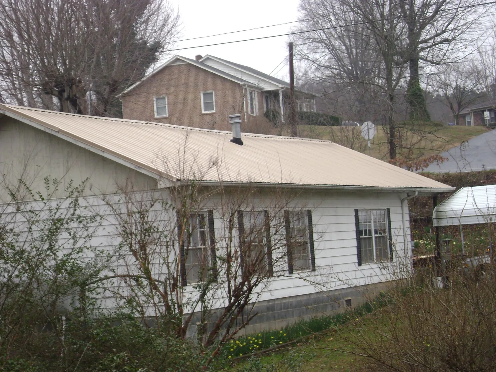 Tan metal roof on a white sided house set into a hillside — Commercial Roofing by Roofing Brothers in Astoria